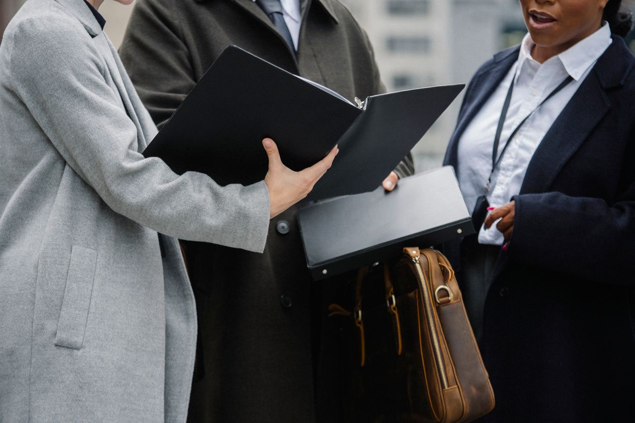 Home Crop diverse coworkers wearing formal outfits reading documents together and discussing project on street