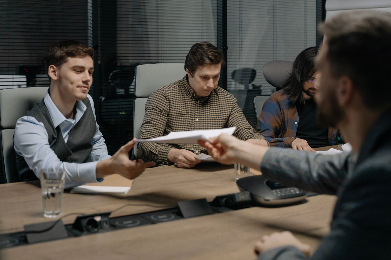 The Art of Drawing Readers In: Your attractive post title goes here Four professionals exchanging documents during a meeting in an office setting.